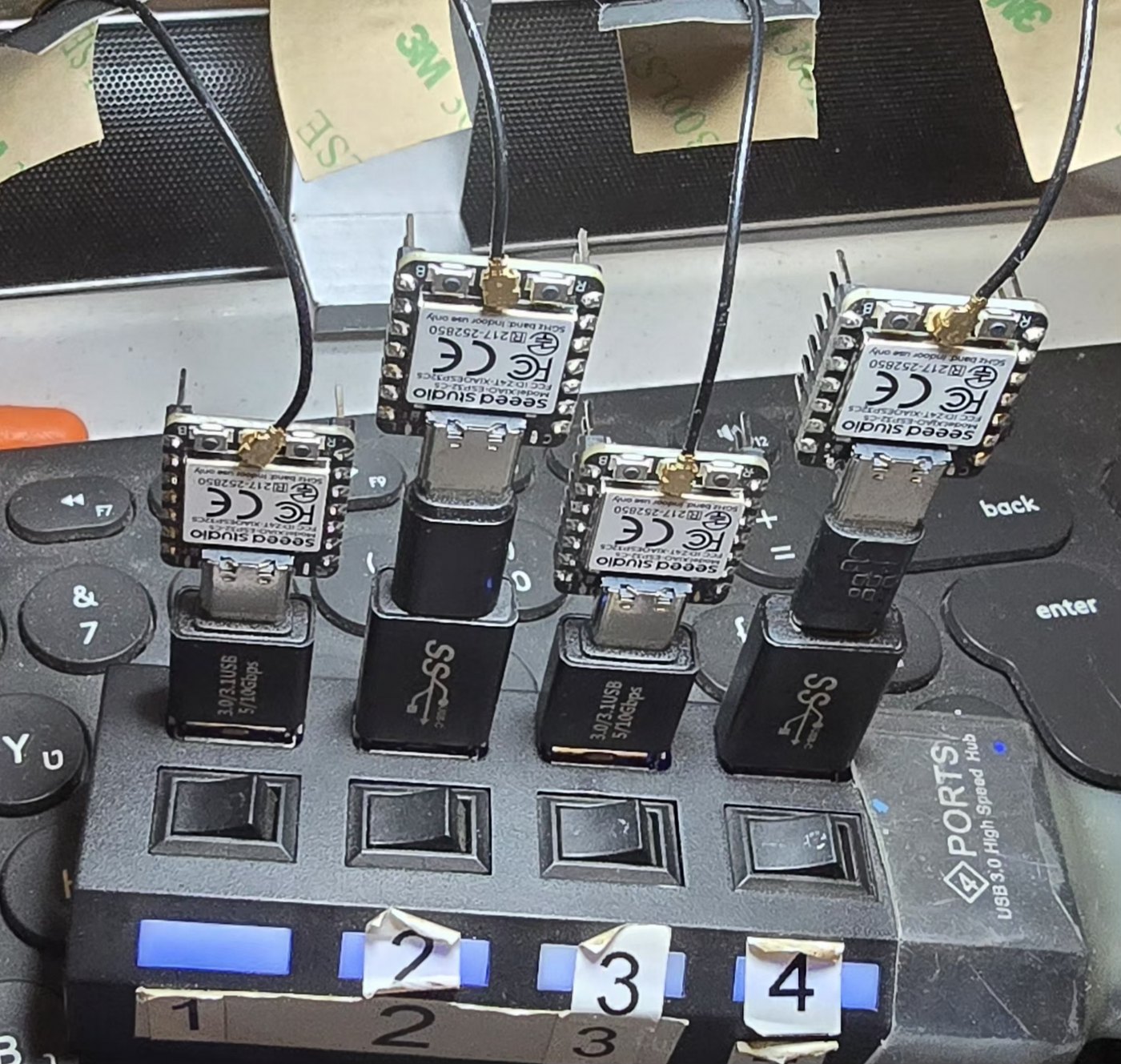 Four Seeed Studio XIAO ESP32C5 boards, each with an external antenna soldered to its u.FL connector, plugged into the four numbered ports of a powered USB 3.0 hub.